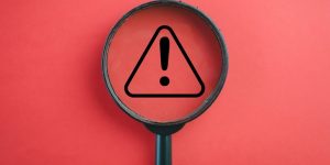 View through a magnifying glass on Exclamation mark or Warning sign over red background Attention sign,Exclamation mark, warning sign concept.