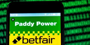 phone displaying the paddy power and betfair logo on screen with a background of code