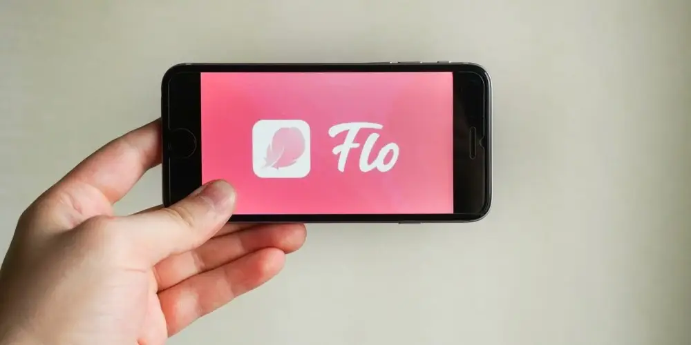Young woman hand holding iphone with logo of Flo application. Flo - is tracking menstruation and menopause, and ovulation calendar.