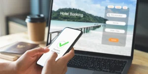 a person holding a phone displaying payment accepted on screen and a laptop with an online travel booking website