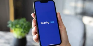 someone holding a phone with the booking.com logo displaying on screen with a homely background