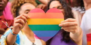 A group of LGBTQ people holding a rainbow heart celebrating International Pride Month.