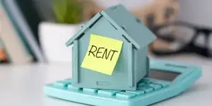 Model house placed on calculator and sticker text Rent. The house has a red roof, It visually represents the concept of renting property