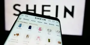 Smartphone with website of fashion e-commerce company Shein in front of business logo