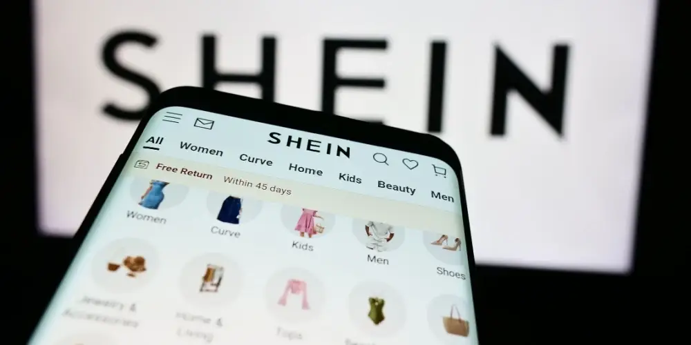 Smartphone with website of fashion e-commerce company Shein in front of business logo