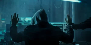 A hooded person in a room full of computers is being arrested
