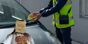 Traffic warden in the UK puts a parking fine ticket on the window of a car and an image of zoe bread - a girl with a bread mask on her face